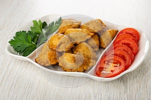 Partitioned dish with patties, leaves of parsley, tomato on wooden table