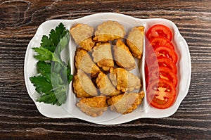 Partitioned dish with patties, parsley, tomato on wooden table. Top view