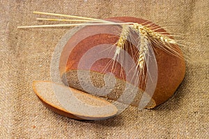 Partly cut brown bread and three wheat ears on sackcloth