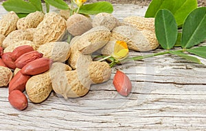 Partly peeled peanuts with leaves and flowers on wooden surface