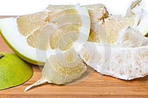 Partly peeled pieces of ripe pomelo on wooden cutting board