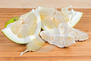 Partly peeled pieces of ripe pomelo on wooden cutting board