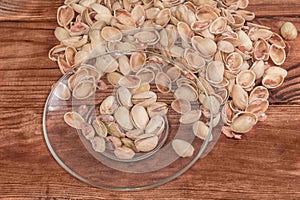 Partly peeled pistachio nuts on transparent saucer against empty shells