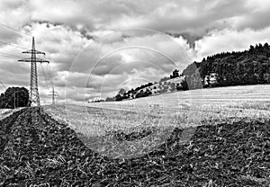 Partly ploughed field after the harvest with transmission tower and wooded hill in the background
