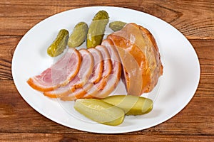 Partly sliced boiled-smoked pork knuckle, pickled cucumbers on plate
