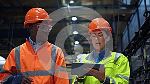 Partners holding tablet computer walking at huge modern manufacturing storage.