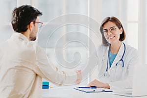 Partnership, assistance, trust and medicine concept. Female doctor shakes hands with thankful patient for good treatment and