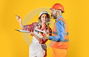 Partnership. Builder Couple Look At Home Plans. couple looking at a blueprint. woman and man wear safety hardhat. family