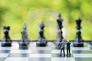 Partnership and teamwork in business strategy concept, two miniature people businessmen work as team, standing on chessboard look