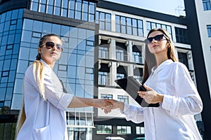 Partnership. Two young business ladies handshaking outside office building