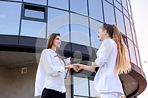 Partnership. Two young business ladies handshaking outside office building