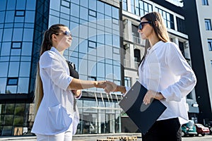 Partnership. Two young business ladies handshaking outside office building