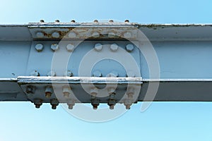 Parts of a modern metal bridge in close-up against a blue sky background. Metal structures connected by large bolts and nuts to a