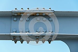 Parts of a modern metal bridge in close-up against a blue sky background. Metal structures connected by large bolts and nuts to a