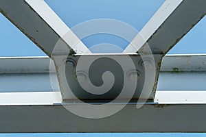 Parts of a modern metal bridge in close-up against a blue sky background. Metal structures connected by large bolts and nuts to a