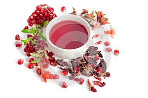 Parts of a pomegranate with pomegranate seeds and leaves, flowers, dry tea of carcade and full cup of tea on white