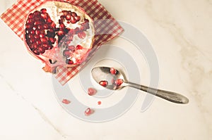 parts of pomegranate on a red napkin and a spoon/ parts of pomegranate on a red napkin and a spoon on a white table, top view