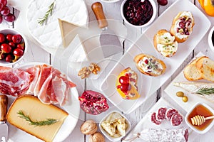 Party appetizers of assorted cheeses, meats and crostini, top view on white wood