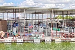 Party-boat covered dock on lake with expensive luxury speedboats docked and chairs and tables and toys for fun and guests in