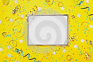 Party, carnival or birthday background decorated silver frame with colorful confetti and streamer on yellow table top view.