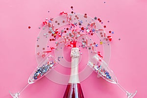 Party with champagne bottle, glasses and colorful party streamers on pink background top view