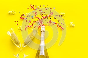 Party with champagne bottle, glasses and colorful party streamers on yellow background top view