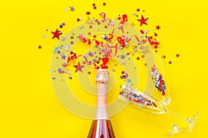 Party with champagne bottle, glasses and colorful party streamers on yellow background top view