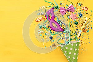 Party colorful confetti and clown hat over yellow wooden background . Top view, flat lay.