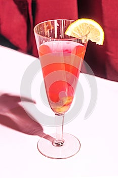 Party concept made of unique, luxurious crystal glass with red cocktail with lemon attached. Lovely burgundy velvet and pink