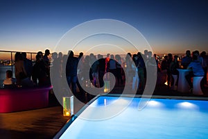 Party crowd of people having fun at roof top club with pool at sunset