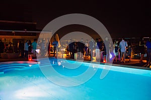 Party crowd of people having fun at roof top club with pool at sunset