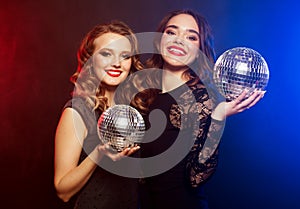 party, emotion and people concept: Two women with disco balls over blue background