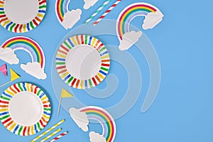 Party flat lay with colorful plates, rainbow napkins and drinking straws on blue background
