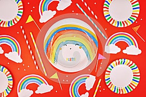 Party flat lay with colorful plates, rainbow napkins and drinking straws on red background