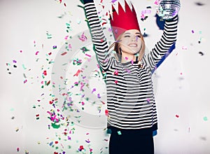 Party girl in colorful spotlights and confetti smiling on white background celebrating brightful event, wears stripped