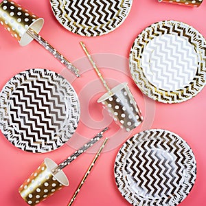 Party golden and silver paper glasses, dishes and straws, party horns on a table.