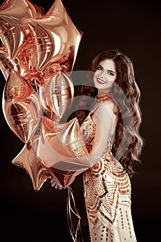 Party. Happy brunette girl with golden star balloons wears in elegant dress isolated on black studio background.