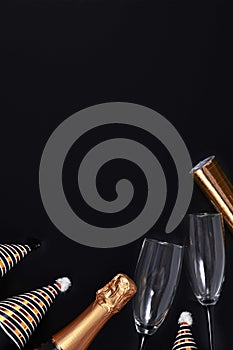 Party hat, champagne bottle head and glasses, and golden paper streamers at bottom of dark black background with  copy space