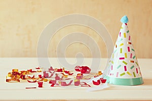 Party hat next to colorful confetti on wooden table.