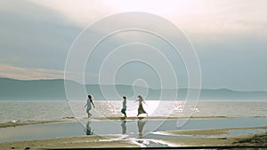 Party and people concept - group of smiling teen girls jumping on beach. Silhouette of three young women running around