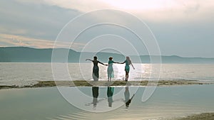 Party and people concept - group of smiling teen girls jumping on beach. Silhouette of three young women running around