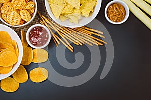 Potato chips and snacks on black slate table, top view