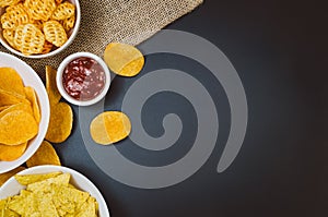 Potato chips and snacks on black slate table, top view