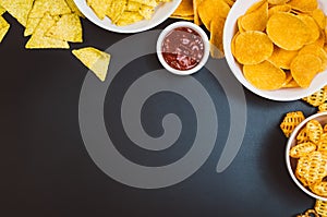 Potato chips and snacks on black slate table, top view