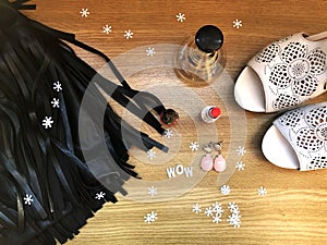Party style flat lay on wooden background. Black leather skirt with fringe, white shoes on heels, perfume, red lipstick, red nail