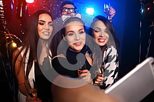 Party, technology, nightlife and people concept - smiling friends with smartphone taking selfie in club.