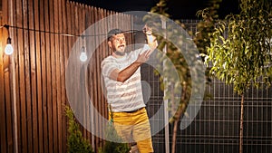 Party time in backyard with happy man hanging string lights in trees