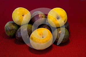 Pasiflora fruits and large yellow plums on red cloth napkin background, selective focus
