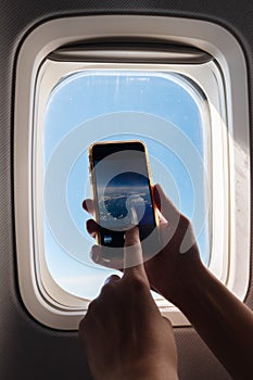 A passanger is taking photo with her smartphone in airplane and watching the view from window.