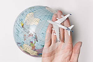 Passenger aircraft on the female palm on the background of the globe. Concept of air travel on a light background